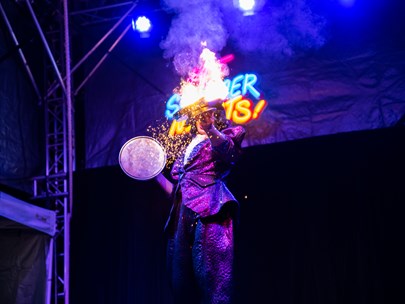 Circus performer on stage playing with fire with neon lights behind them.
