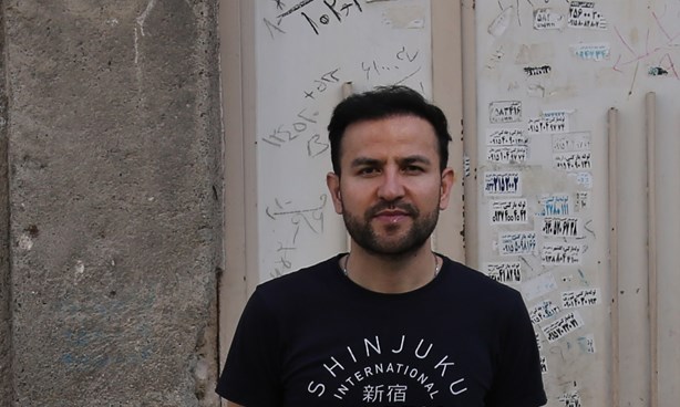 Elyas Alavi Headshot standing in front of a dilapidated building