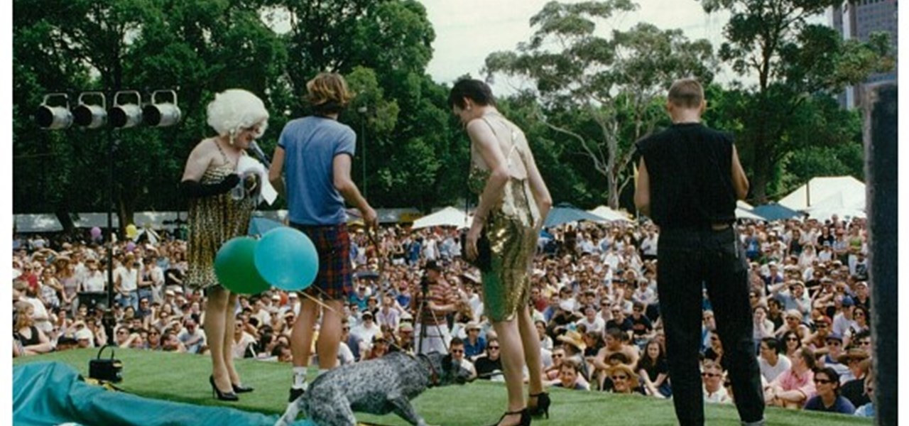 Midsumma Carnival 1996 by Richard Israel and 1997 by Virginia Selleck: four people (including Dulcie du Jour) on stage with the audience in the background