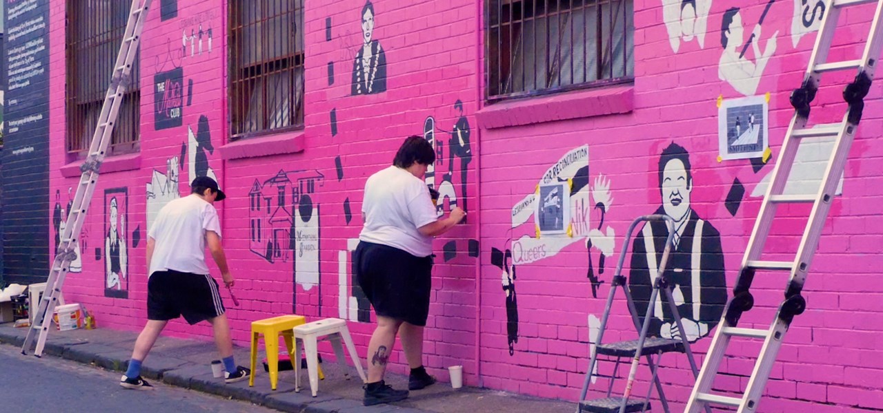 People painting the Queerways mural in pink and black tones