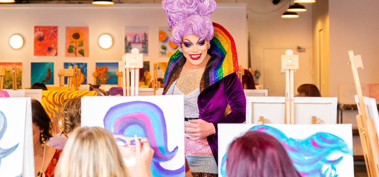 Drag queen with a very tall mauve wig surrounded by artists creating paintings on easels