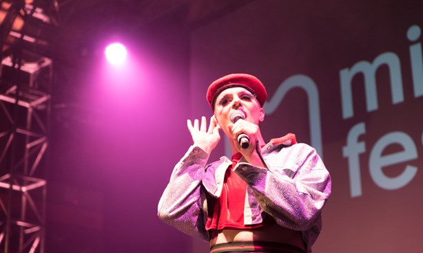 Reuben Kaye holding a microphone, with one hand to their ear