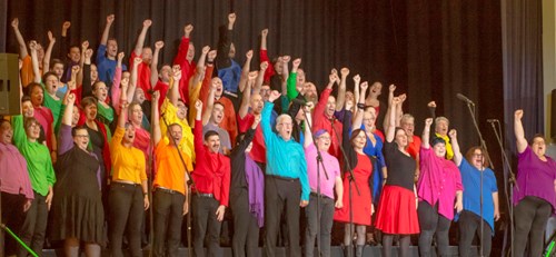 Colourfully dressed large choir with everybody holding their hands in the air