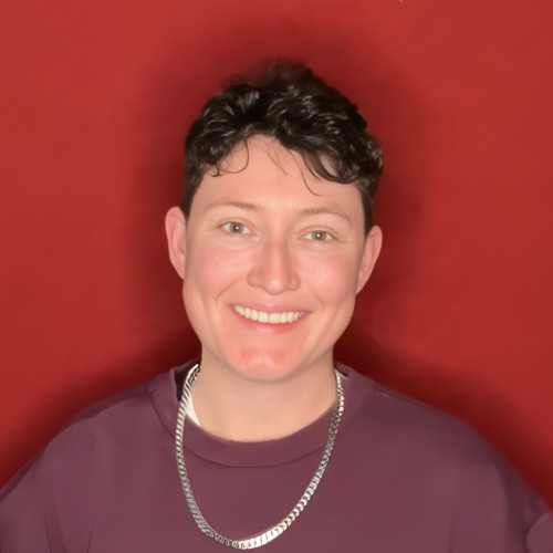 Headshot of Carrie against a red-brown background wearing a silver necklace and a mauve top