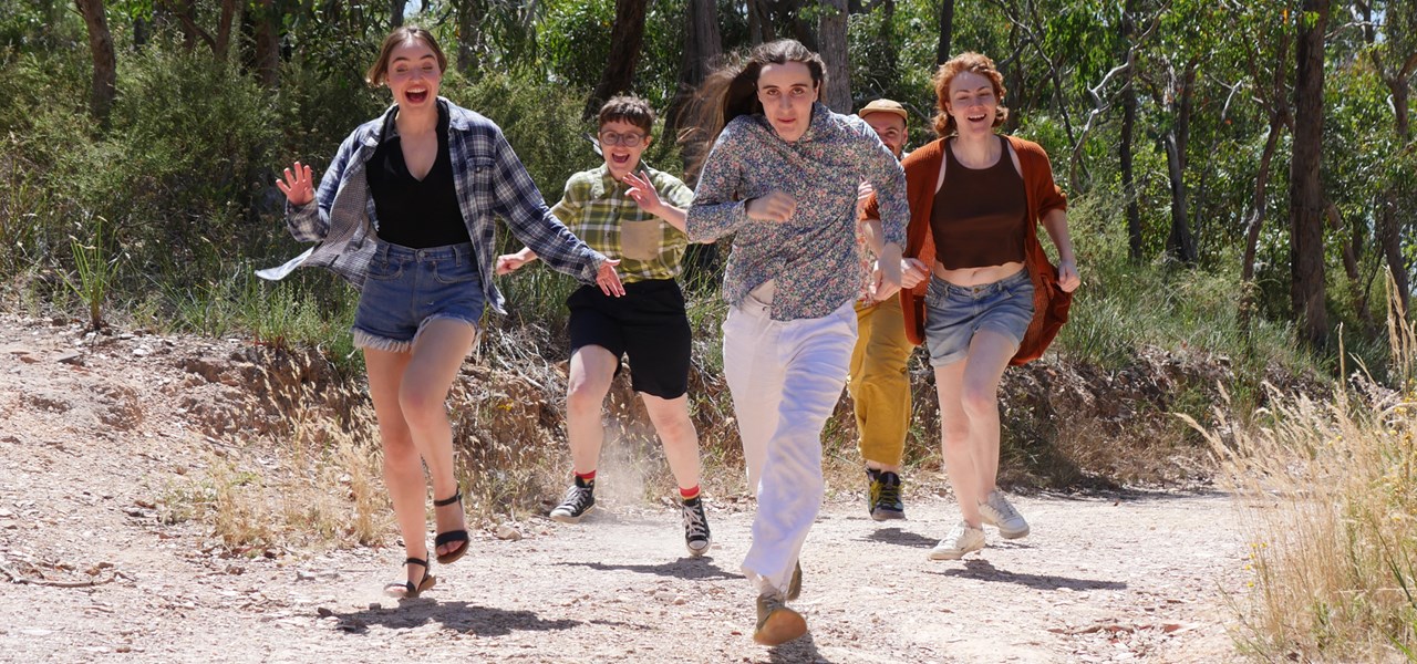 A group of young adults are running through a park, surrounded by trees.