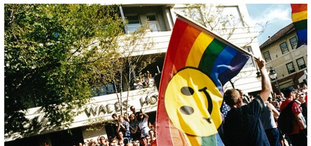Pride March 2000 image: a person waving a large rainbow flag with a "happy person" emoji on it