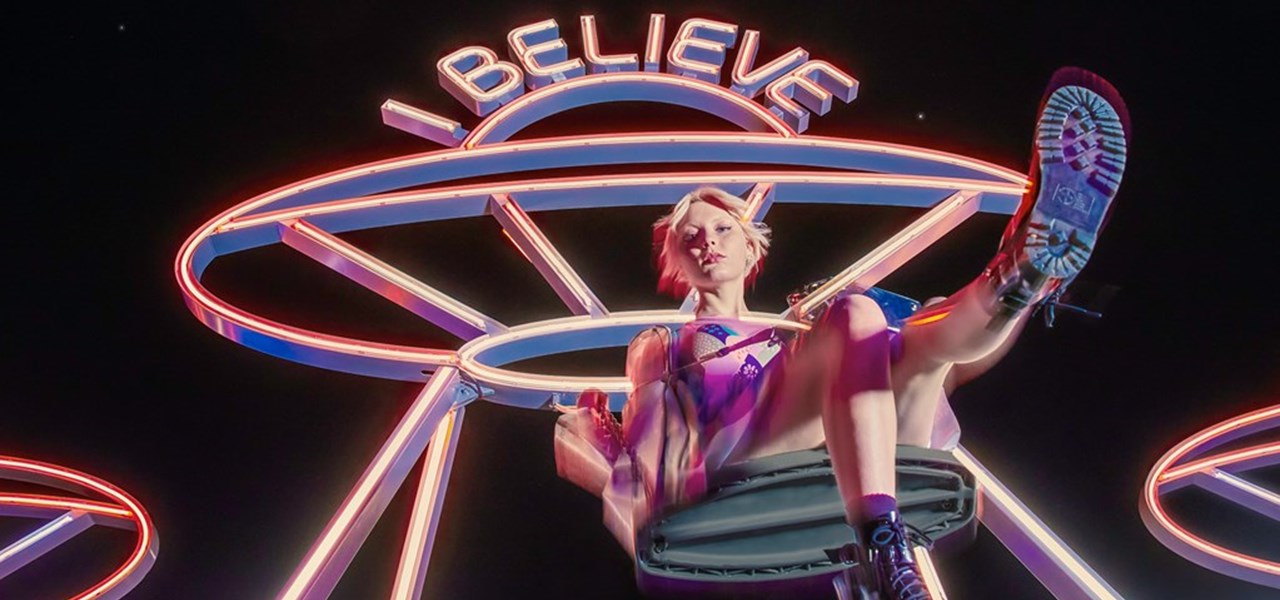 Skateboarder "suspended" in front of a neon sign saying 'I believe'