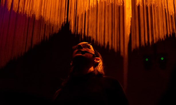 A person is standing in a venue in front of orange light and is looking up. 
