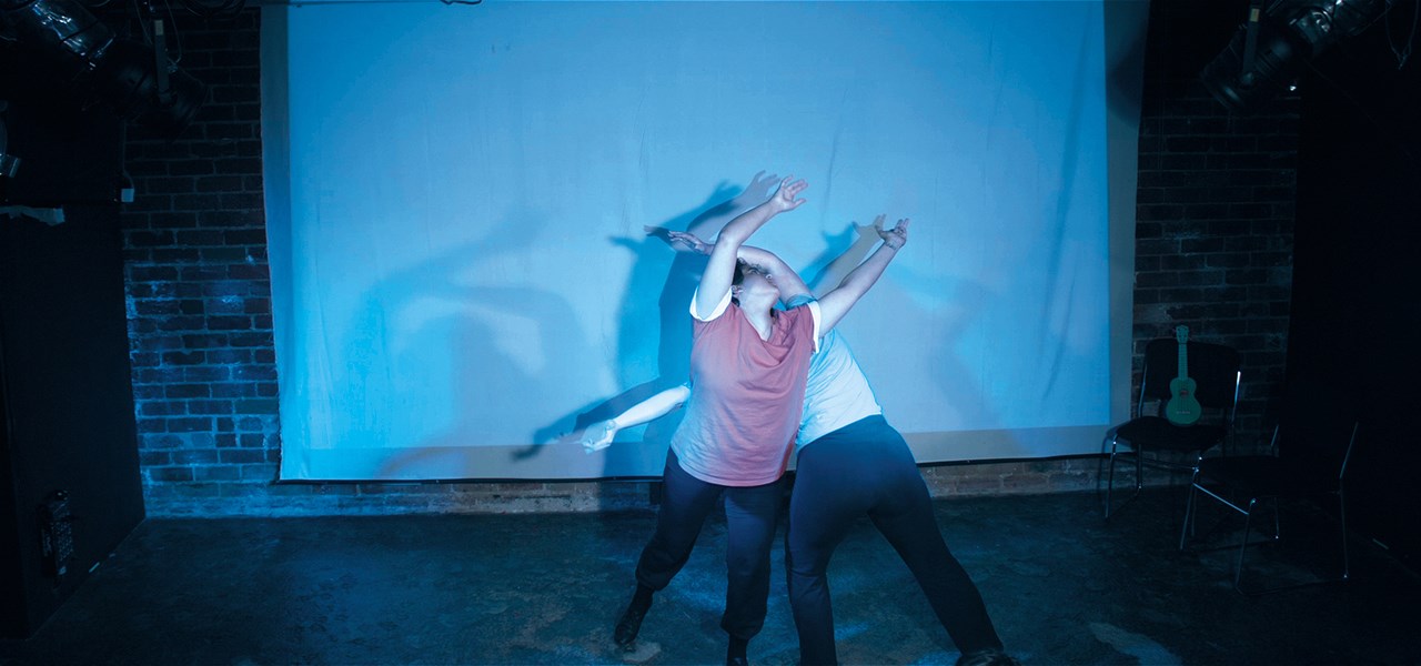Solar (Neptune Henriksen) and Dylan (Lou Sebial) are lifting arms up, back-to-back, in a twist. Solar is facing audience, Dylan is facing away.