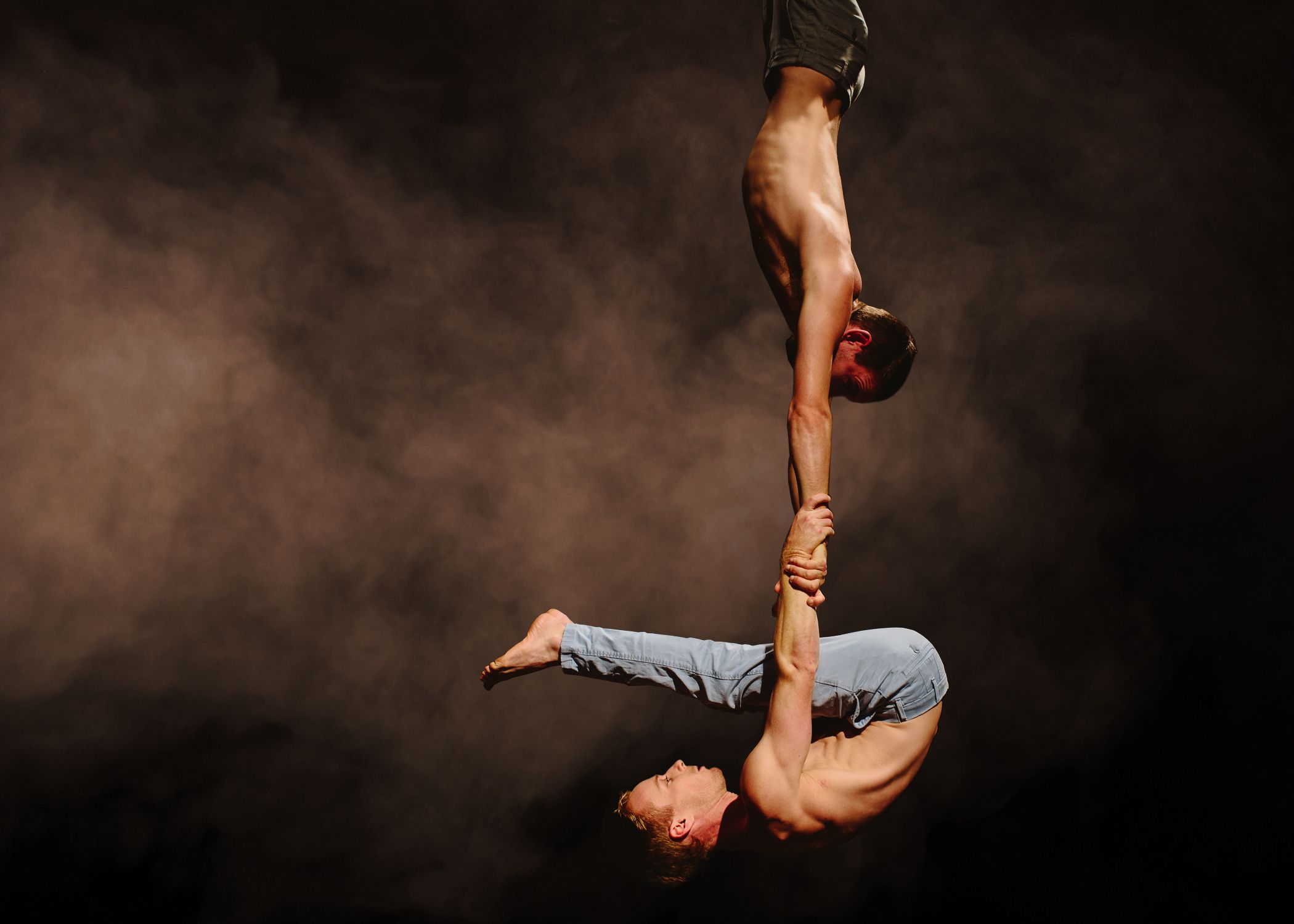 Two hanging bare-chested circus performers, one holding the other