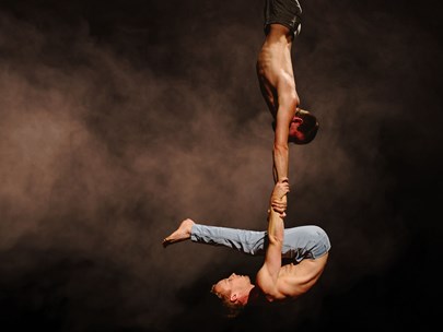 Two hanging bare-chested circus performers, one holding the other