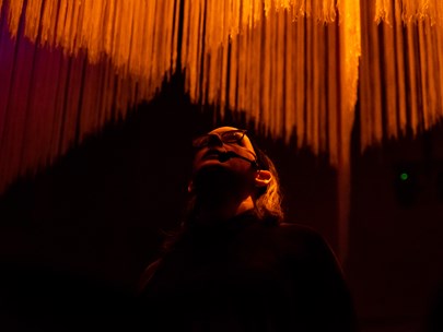 A person is standing in a venue lit up in orange against a hanging display and is looking up. 