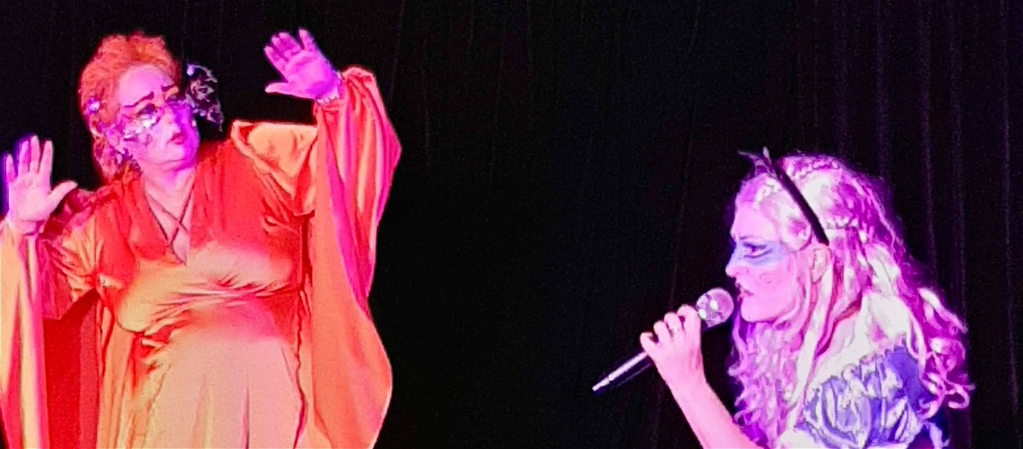 Madam Nightingale in red dress surprised by Cloutie Will singing with mic in Alice costume.