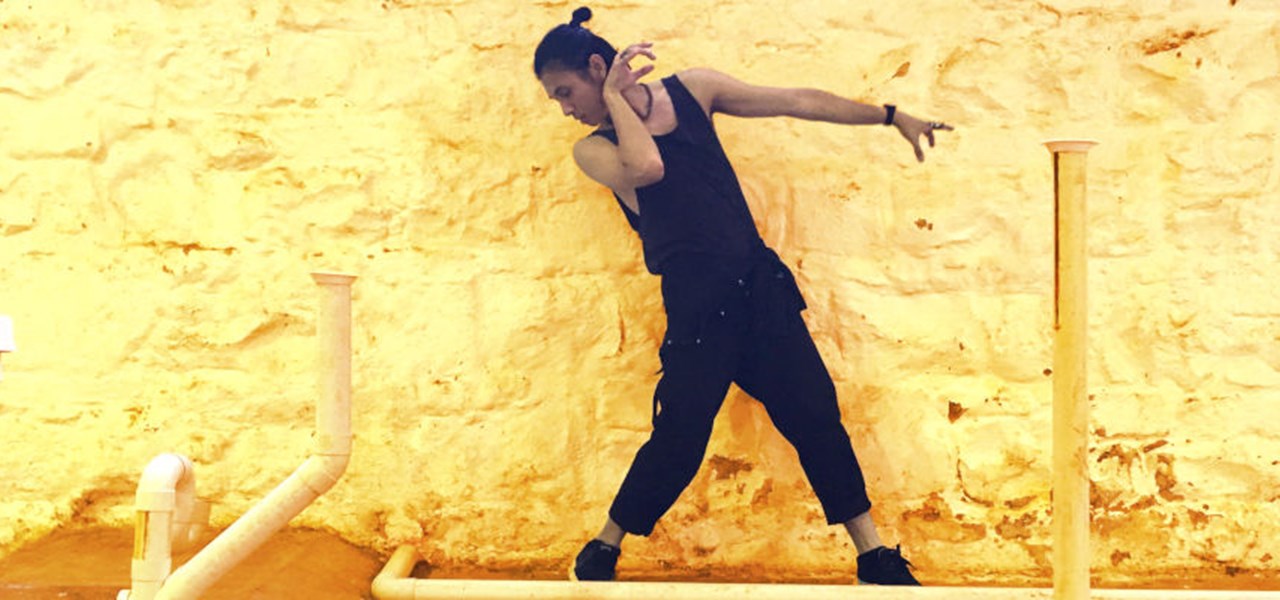 Dancer dressed in black against a yellow-painted, rather rough wall