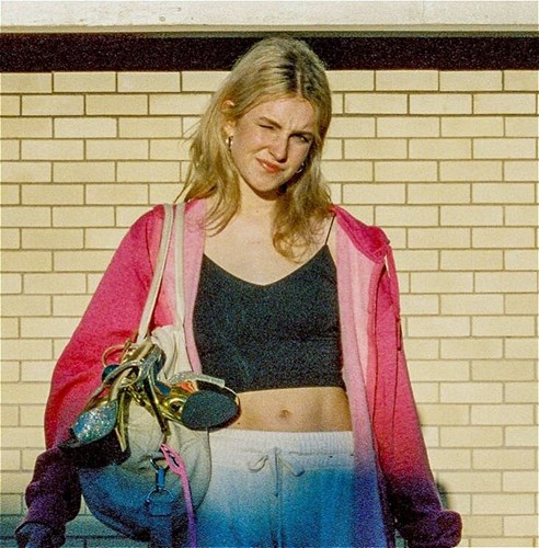 Person standing in front of a cream-brick wall with a wistful expression, bag slung over one shoulder