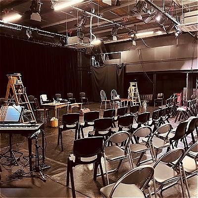 A black box theatre with folding chairs facing a stage and lighting rig.