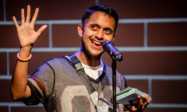 Happy looking person waving while standing in front of a microphone and holding some "cue cards"
