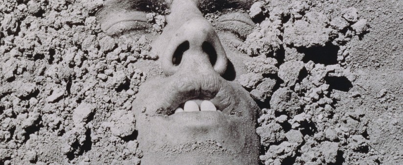 Person buried in sand/mud, with just their eyes, mouth and nose exposed
