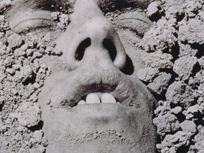 Person buried in sand/mud, with just their eyes, mouth and nose exposed