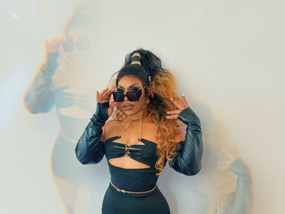 Kween Kong in black outfil, holding their sunglasses, with several 