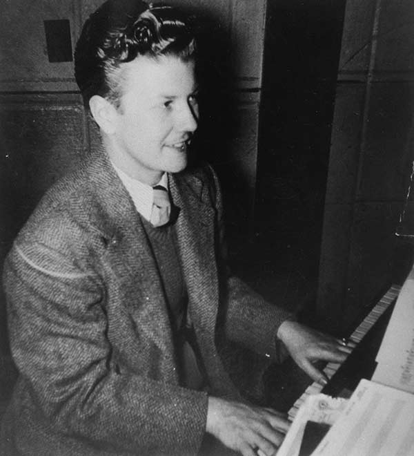 Black and white photo of a smiling man playing a piano