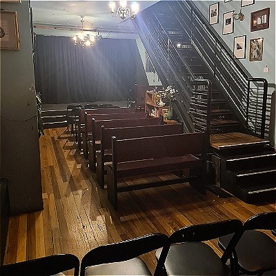 Dark venue with a stage in the background, chairs in the foreground and staircase on the right