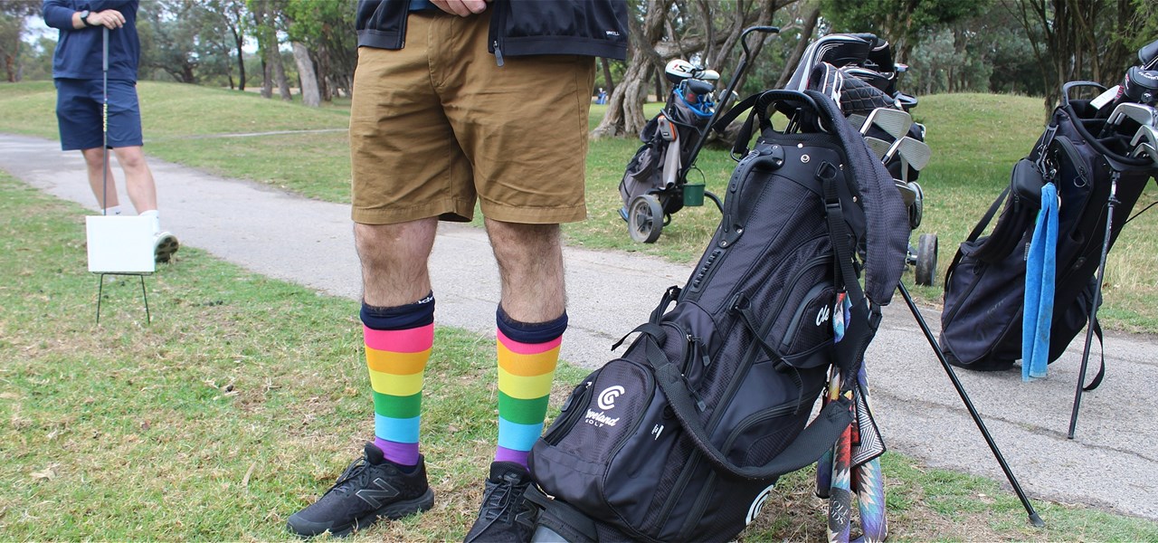 A person wearing knee-high rainbow socks stands next to a golf caddy