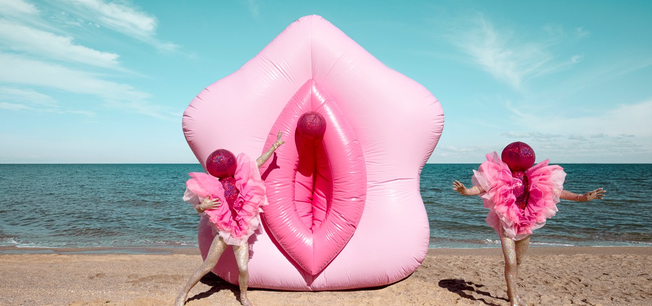 The Huxleys on a beach, dressed in pink, in front of a giant, plastic pink inflatable vulva