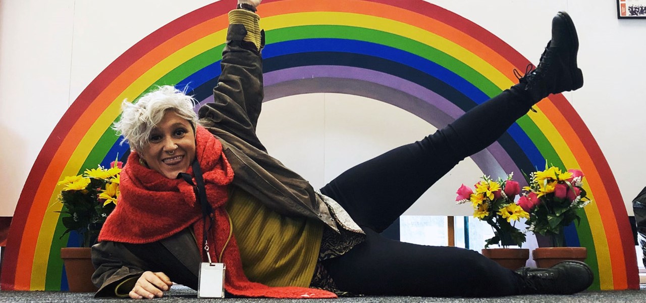 Sasha Catalano lying on the floor in front of a large rainbow arch
