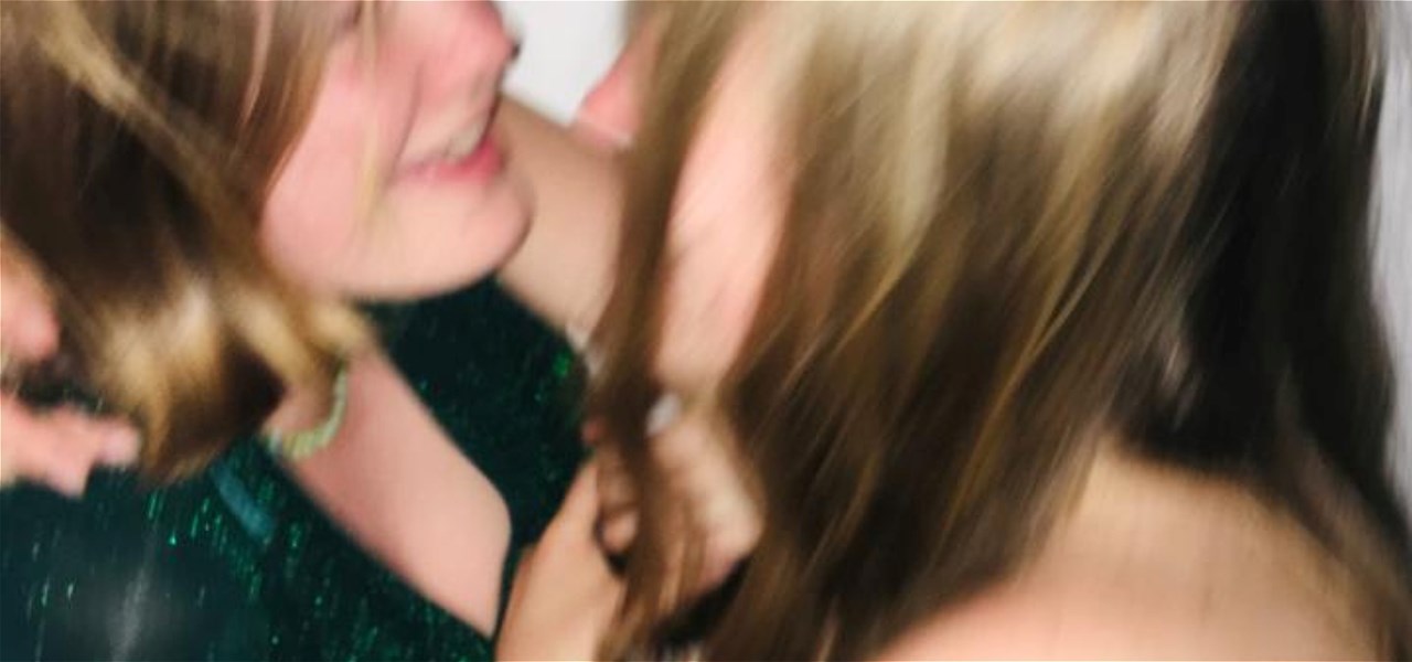 A motion-blurred image of two people embracing. The one on the left wears a sparkly green dress, and the one on the right is leaning into them.