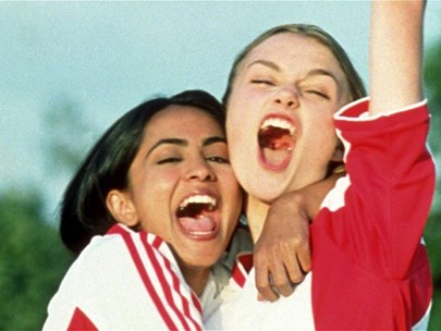 Two teenagers in red and white football jerseys celebrate the scoring of a goal.