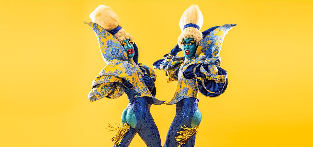 Two performance artists in blonde wigs, platform boots and blue-sequinned bodysuits, with a dynamic pose