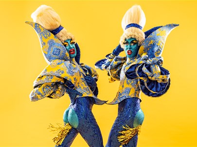 Two performance artists in blonde wigs, platform boots and blue-sequinned bodysuits, with a dynamic pose