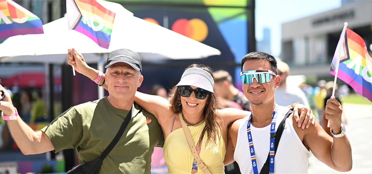 Two male-identifying people holding rainbow AO flags, with a female-identifying person between them with her arms around them