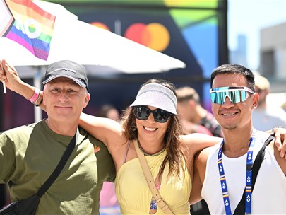 Two male-identifying people holding rainbow AO flags, with a female-identifying person between them with her arms around them