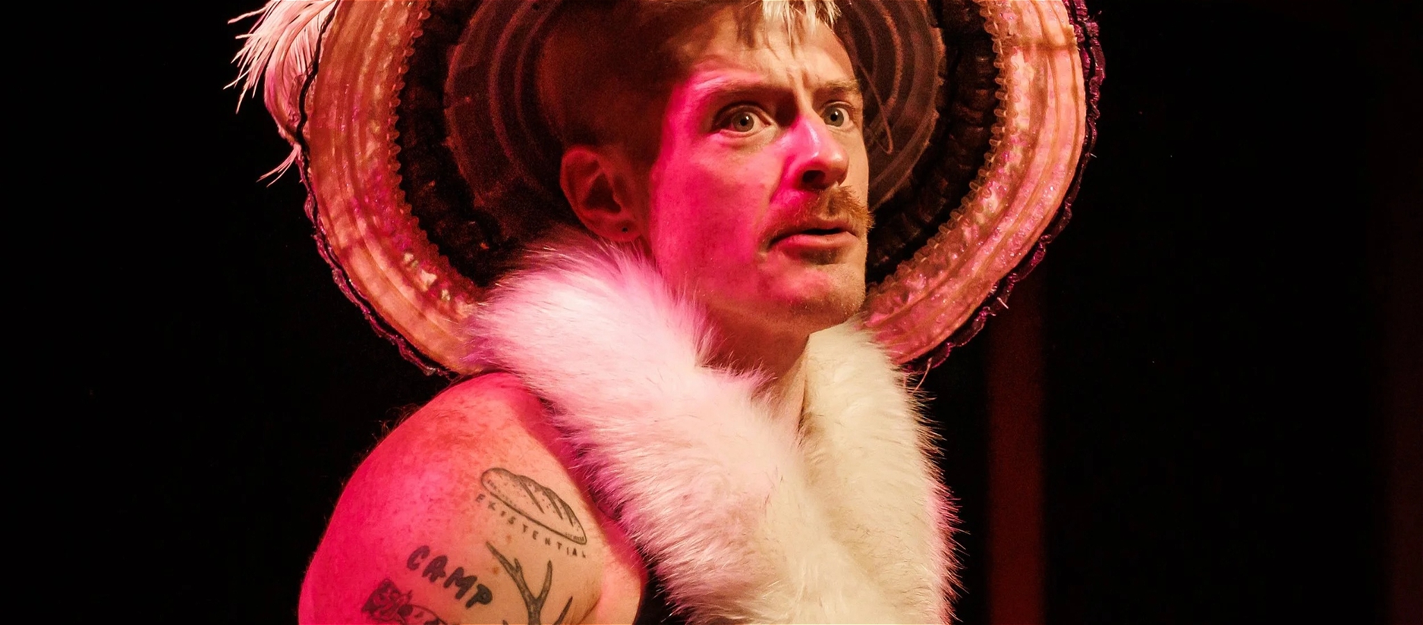 Christopher Bryant wearing a singlet, large-brim hat and a fake fur stole looking worried
