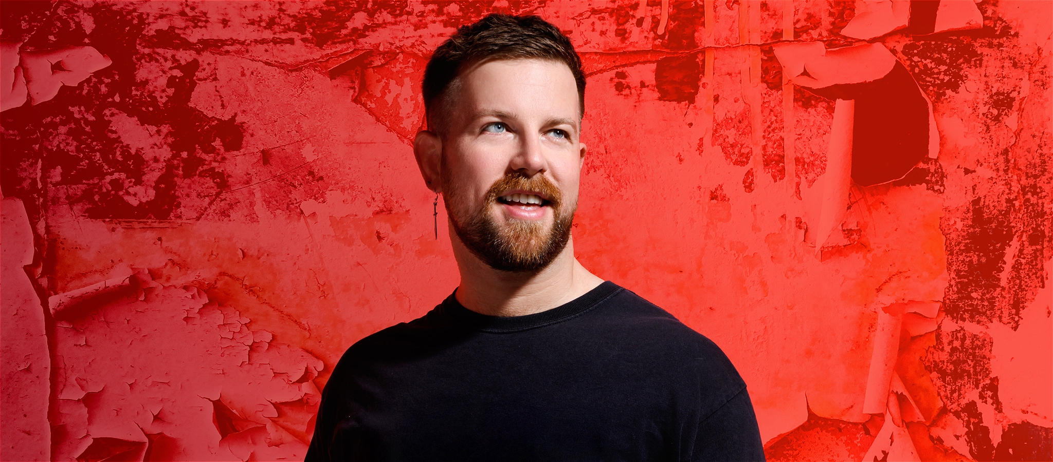 Happy looking bearded young person against a red background