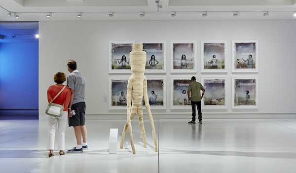 A couple and a single person in a large gallery space; lots of white tones