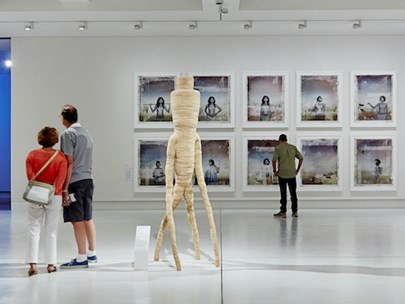 A couple and a single person in a large gallery space; lots of white tones