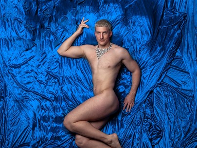 Ziegfeld Boy lies on a bed of royal blue silk sheets wearing nothing but a diamond necklace