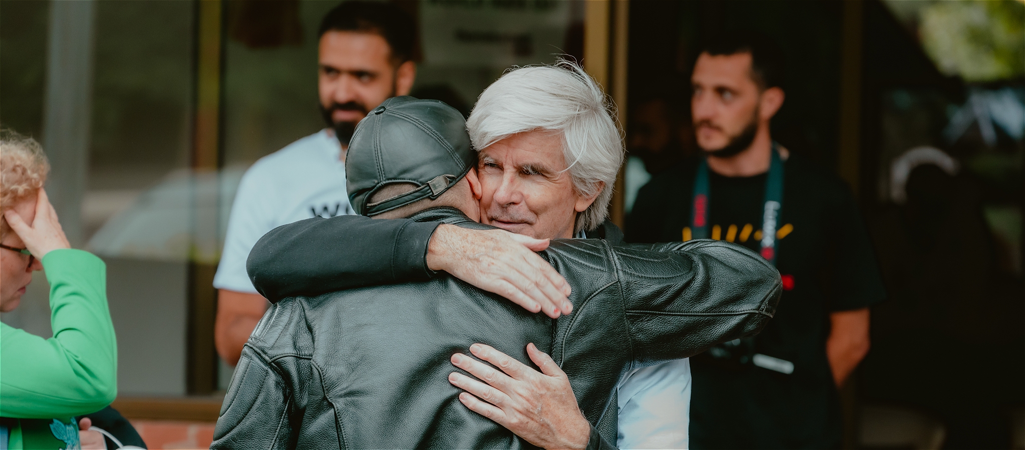 Two men come together outside and are hugging in a happy manner.