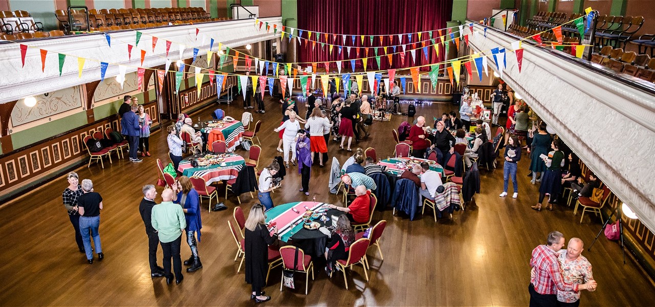 A hall filled with bunting and tables, with a large dancing crowd.