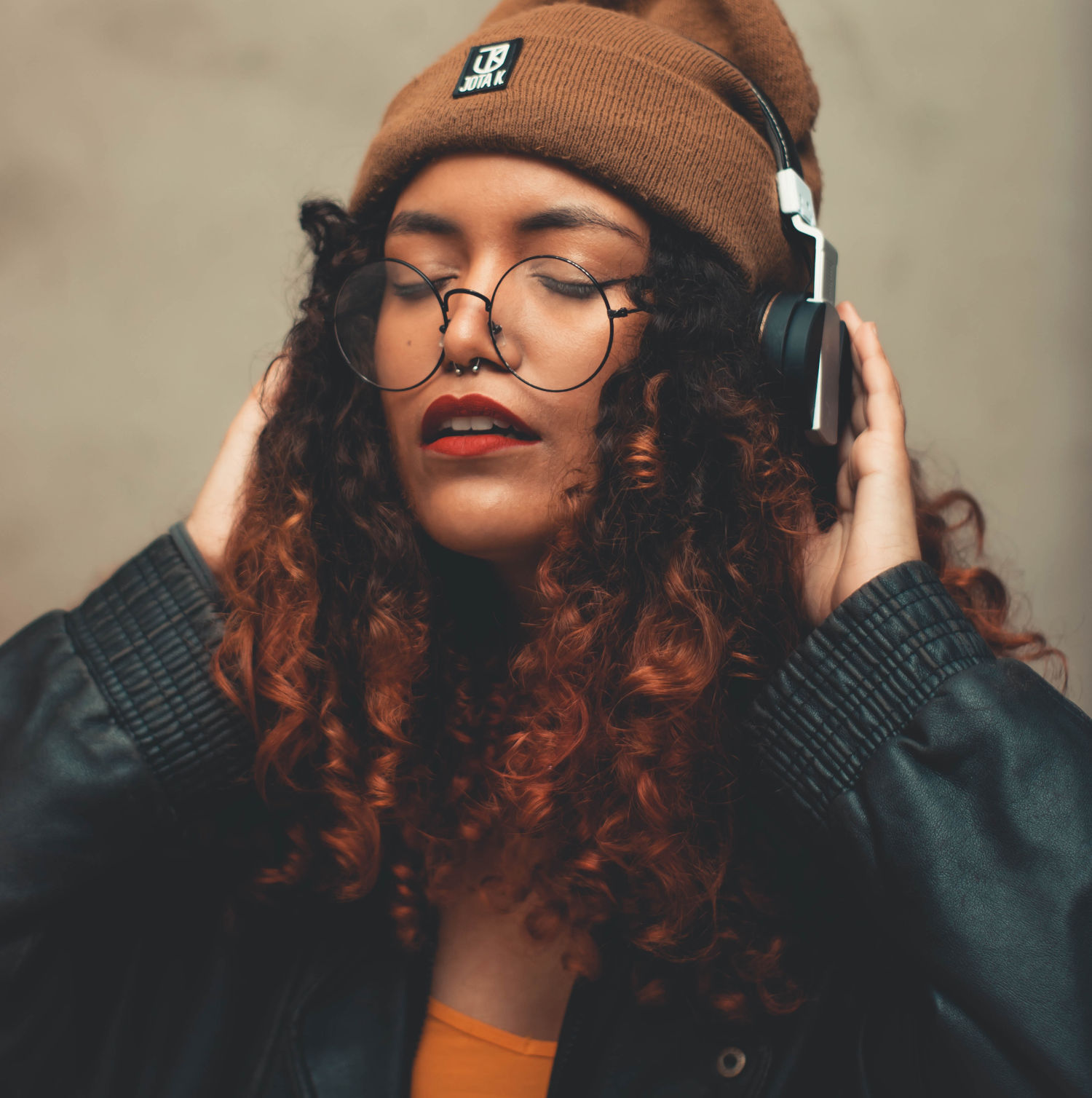 Person wearing a brown beanie listening intently through headphones, hands on the phones