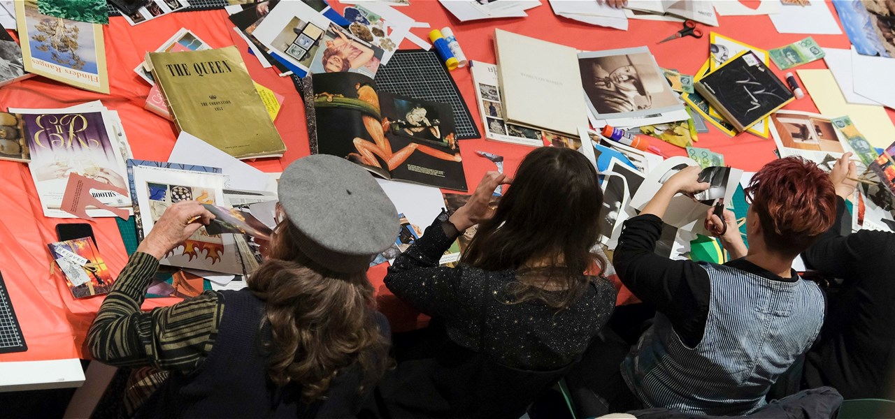 People sitting on a large table full of books and magazines, cutting and making paper collages