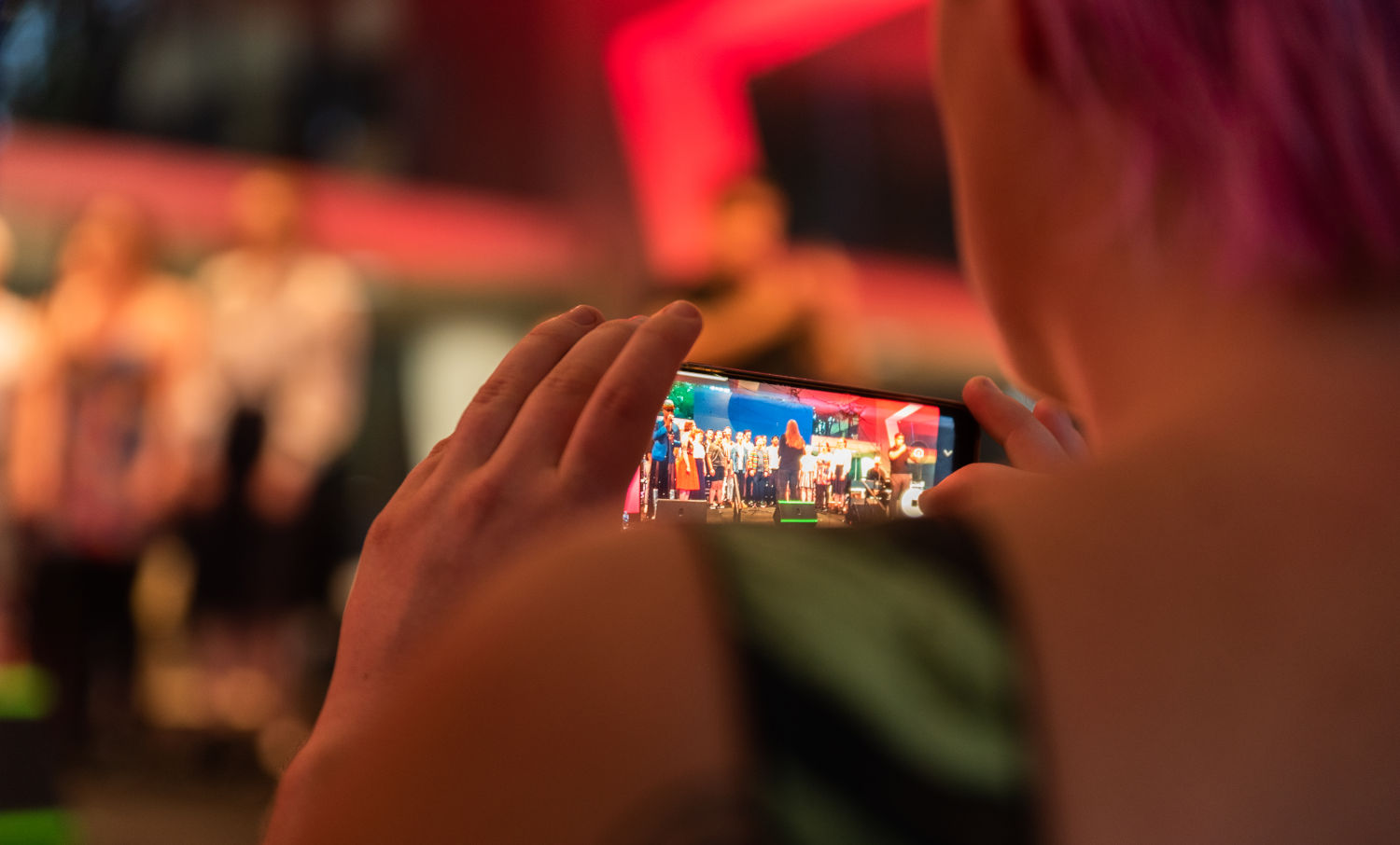 Person taking a photo on their phone of performers on stage - only the phone is in focus