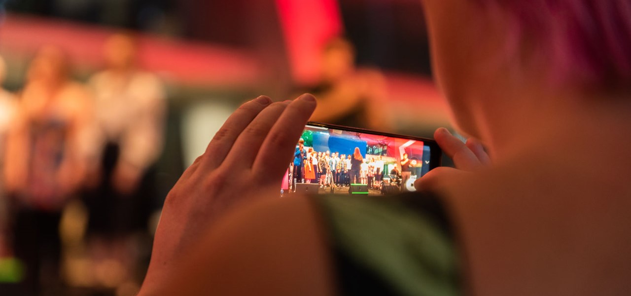 Person taking a photo on their phone of performers on stage - only the phone is in focus