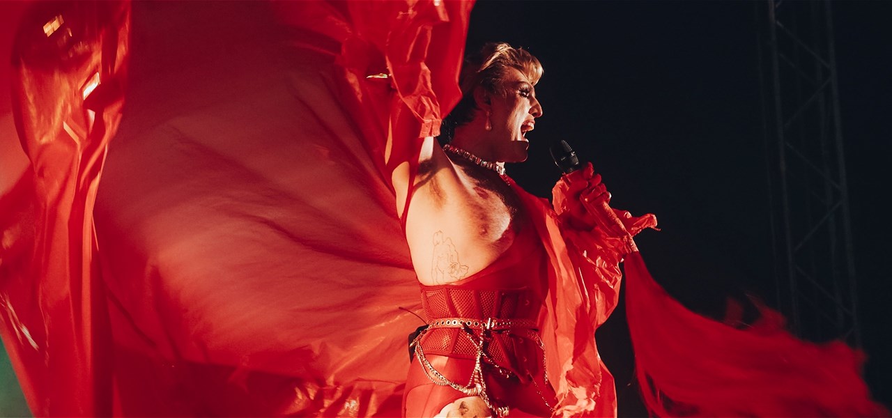 Reuben Kaye dressed in flowing red gown, arms outstretched