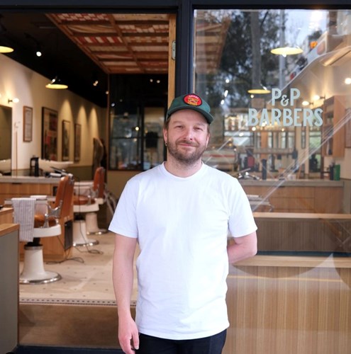 A person standing proudly in front of the P&P Barbers shop