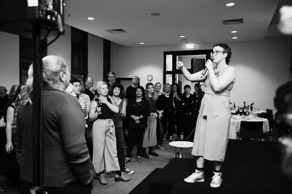 black and white photo of a person on a low stage speaking to an audience