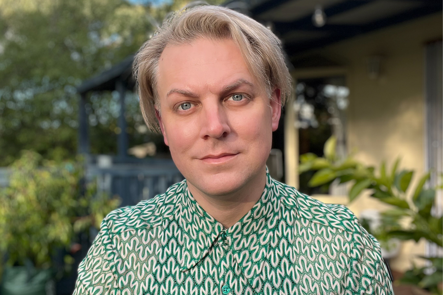 A person with blond hair wearing a green button down.